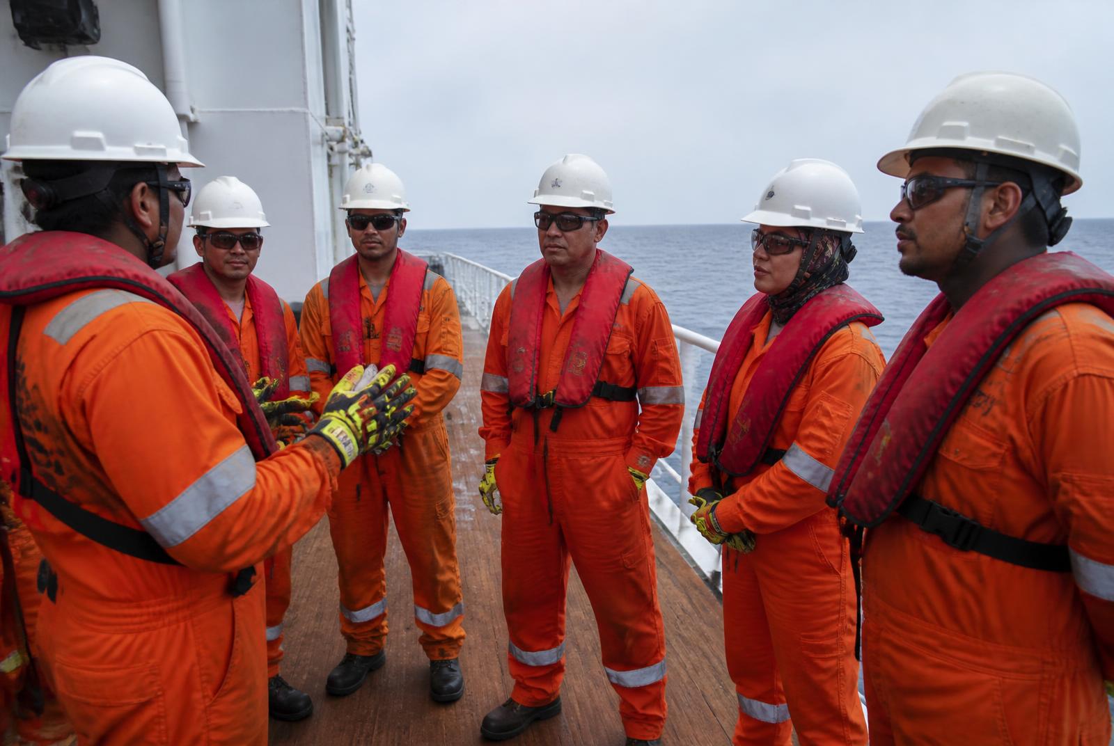 Offshore marine crew in safety gear during a toolbox briefing on a vessel deck
