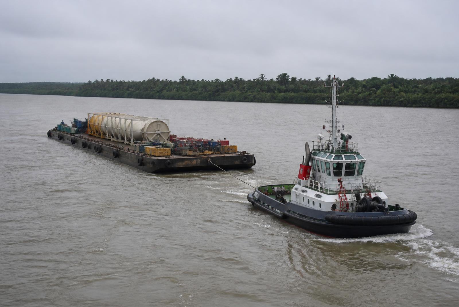 Tugboat towing a loaded cargo barge through a Niger Delta channel